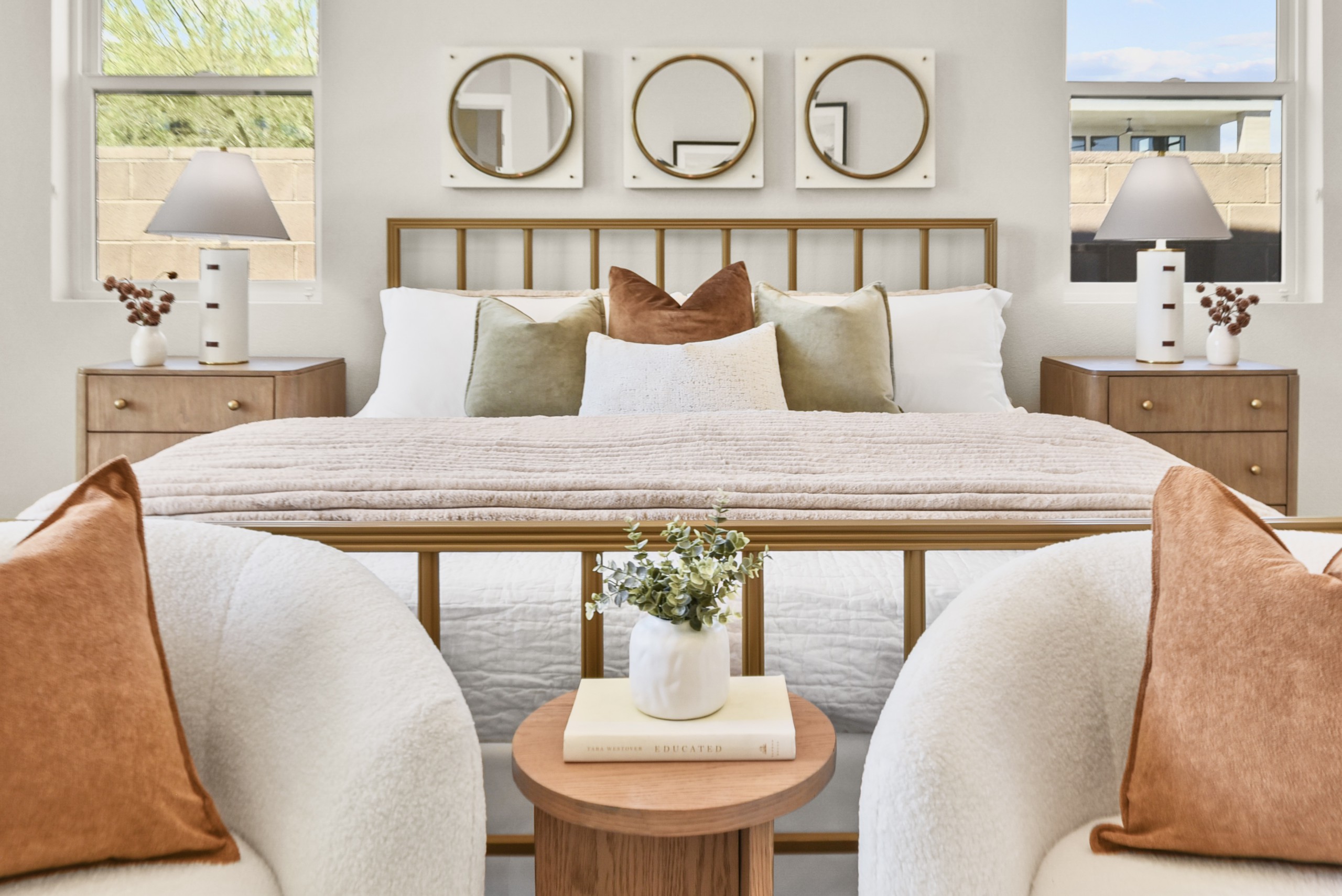 Staged luxury bedroom with brass bed frame, velvet pillows, layered throws, and bouclé accent chairs at Stone View Las Vegas