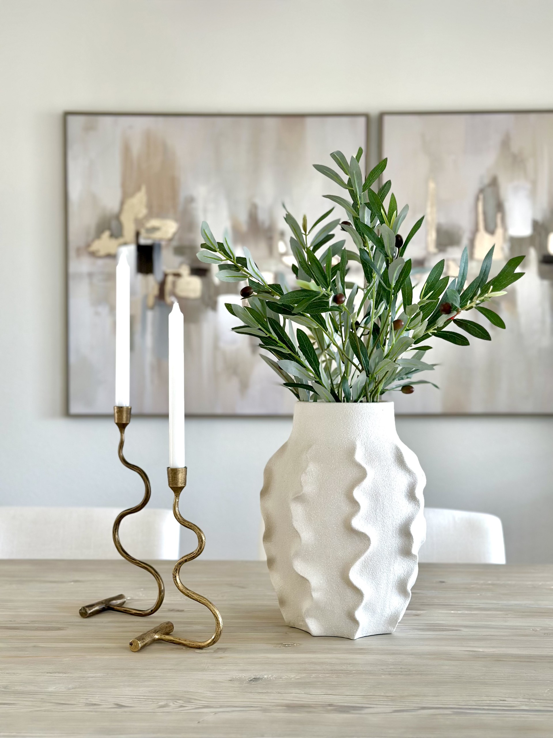Styled dining table vignette with sculptural vase and olive branches showing staging attention to detail